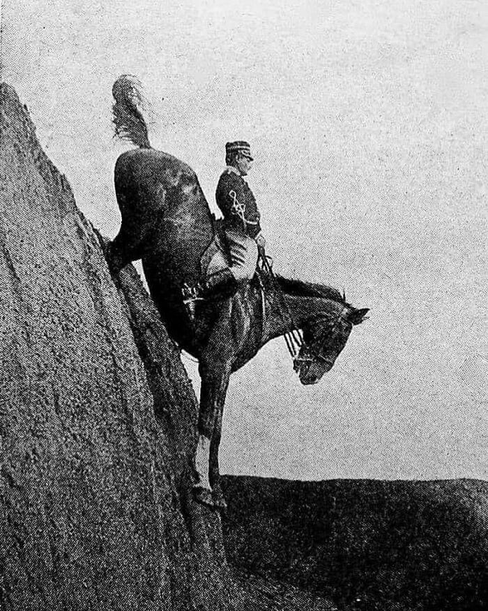 Black and white historic photograph showing a man on horseback descending a steep cliff, illustrating history of humanity.