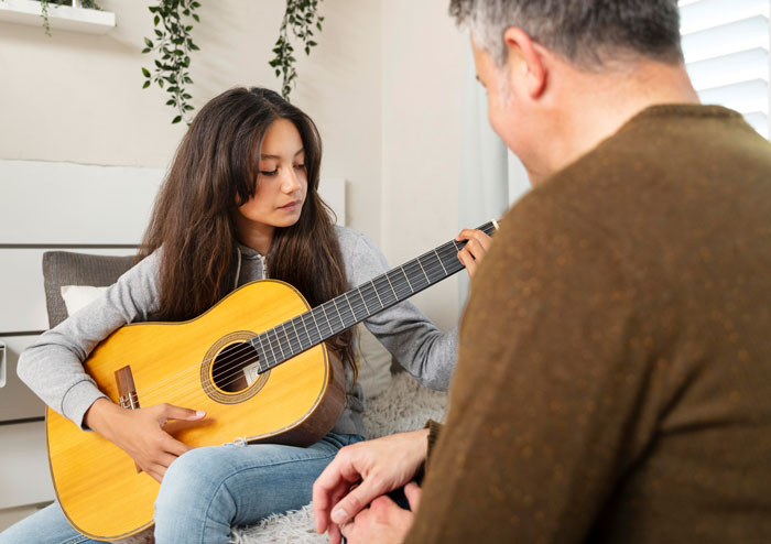 Young woman playing acoustic guitar while a man watches, showcasing moments of people being smart and focused.