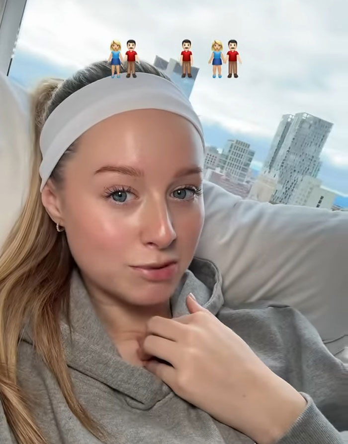 Young woman sharing why she has 7 parents, sitting indoors with emojis of multiple parents above her head. Young woman sharing why she has 7 parents, sitting indoors with emojis of multiple parents above her head.