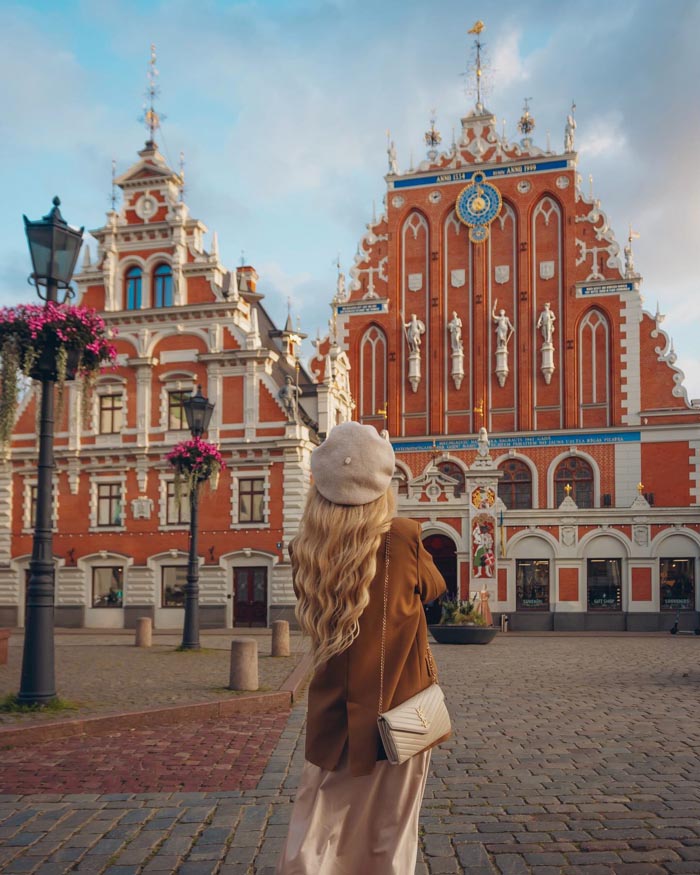 Woman with long hair in a brown outfit standing in front of historic buildings in a country known for sleep patterns from OECD data