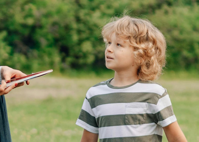 Blonde child with no filter speaking outdoors, revealing family lore in a candid moment teachers didn’t need to know.