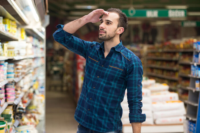Man in a plaid shirt looking confused in a store aisle, capturing a weird and satisfying situation moment.