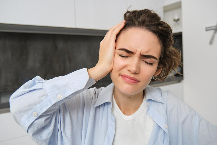 Young woman holding her head in pain, experiencing a moment that hits harder than she'd like to admit.
