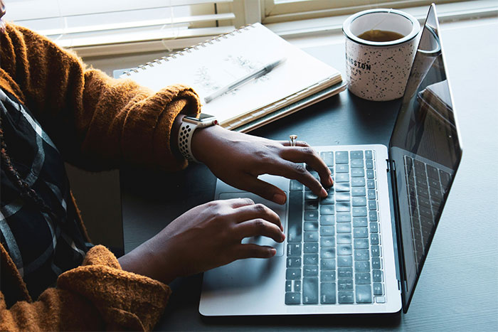 Woman typing on laptop with notebook and coffee nearby, related to coworker filming to prove disability claims.