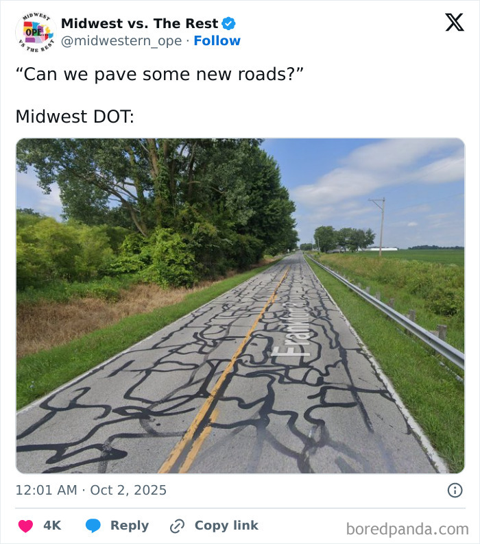 Rural Midwest road covered in numerous black patch repairs surrounded by green fields and trees under a blue sky.
