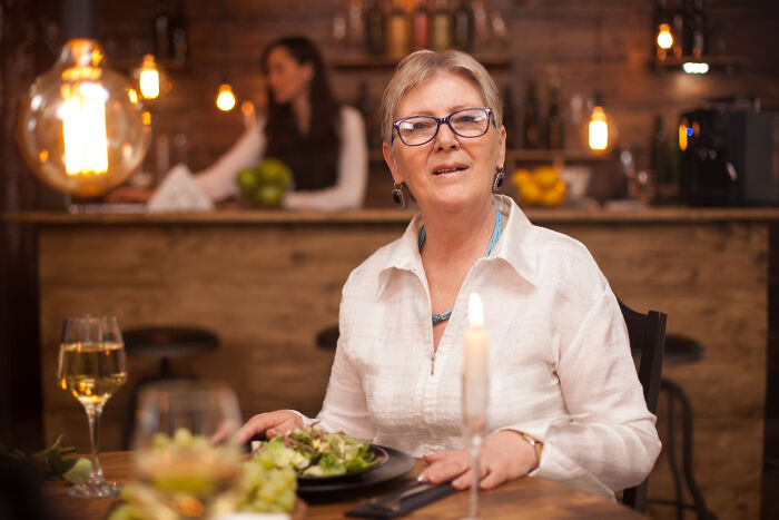 Woman in glasses sitting at a restaurant table with a salad, capturing an awkward moment in the service industry.