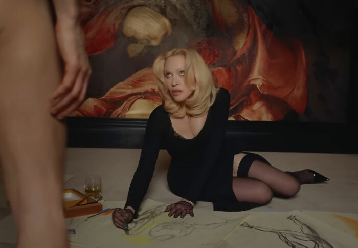 Madonna in a raunchy Dolce & Gabbana ad sketching a male model with a c****h shot, surrounded by younger men. Madonna in a raunchy Dolce & Gabbana ad sketching a male model with a c****h shot, surrounded by younger men.