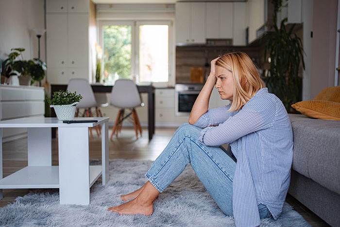 Upset woman sitting on living room floor, holding her head, portraying embarrasses wife moment and domestic tension Upset woman sitting on living room floor, holding her head, portraying embarrasses wife moment and domestic tension