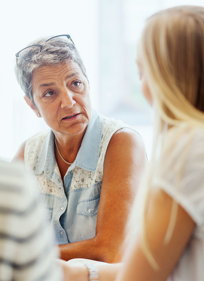 Older woman speaking seriously to younger woman, illustrating tension with mother-in-law and manipulative gift control.