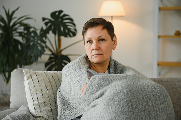 Woman wrapped in a gray blanket sitting on a couch looking concerned, illustrating the woman who hasn&rsquo;t worked since 2006.