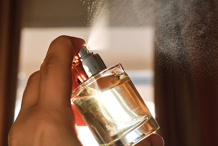 Pulverizando perfume manualmente a partir de um frasco de vidro transparente com névoa visível na iluminação interna quente, a MIL segue o conceito de padre.