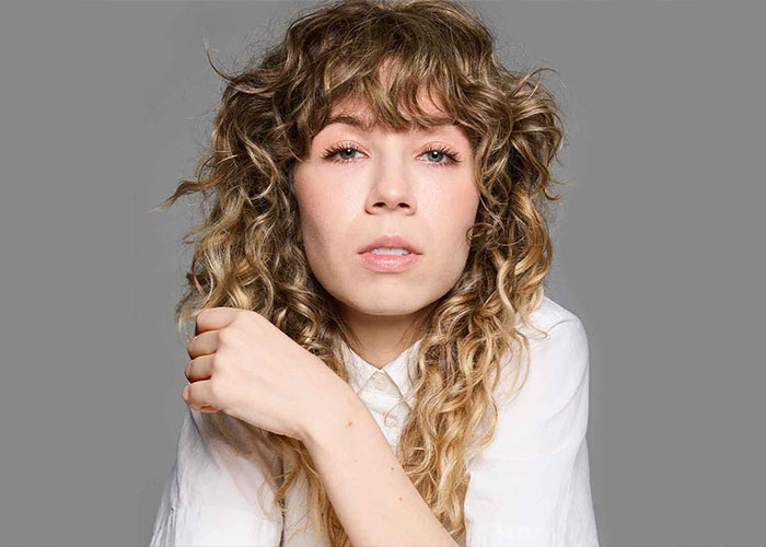 Jennette McCurdy with curly hair in a white shirt, sharing about her twisted and addictive relationship as a teen.