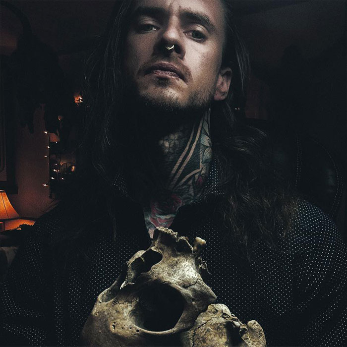 Man with tattoos holding a worn skull in dimly lit room, evoking chilling and horrifying discovery themes.