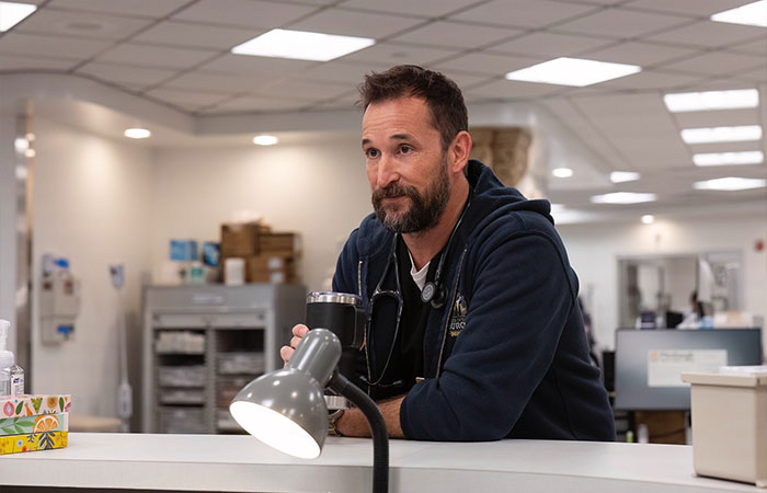 Noah Wyle in a hospital setting, wearing a stethoscope and navy hoodie, portraying a character in The Pitt Season 2. Noah Wyle in a hospital setting, wearing a stethoscope and navy hoodie, portraying a character in The Pitt Season 2.