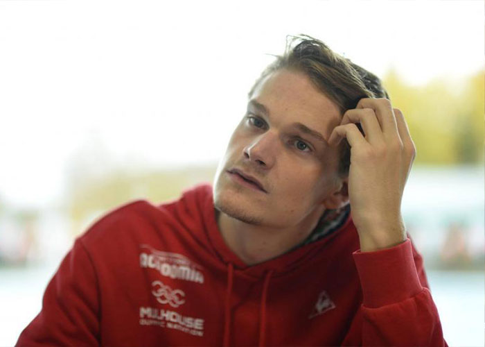 Young man in a red sports hoodie appearing thoughtful, linked to Olympic gold medalist charged with crime news.