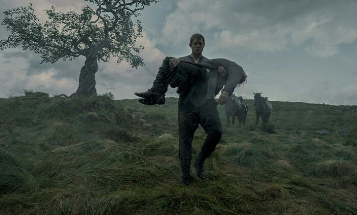Man carrying another on grassy hill with cows nearby, related to Peter Claffey's height mocked by child star Dexter Sol Ansell.
