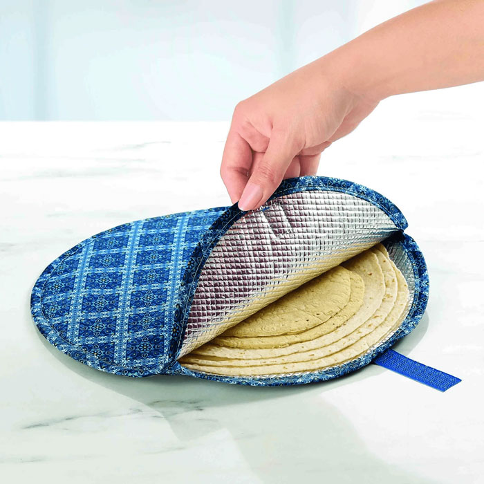 Hand holding a blue patterned household item used to keep tortillas warm, unique to certain countries.