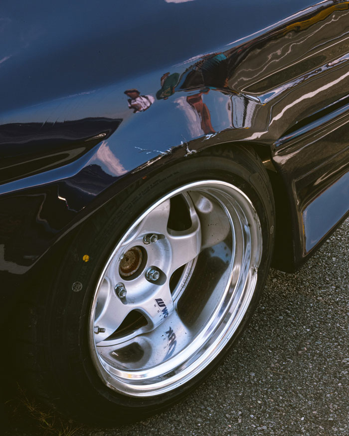 Close-up of a sleek car wheel and reflective bodywork showcasing smart design and craftsmanship on asphalt.