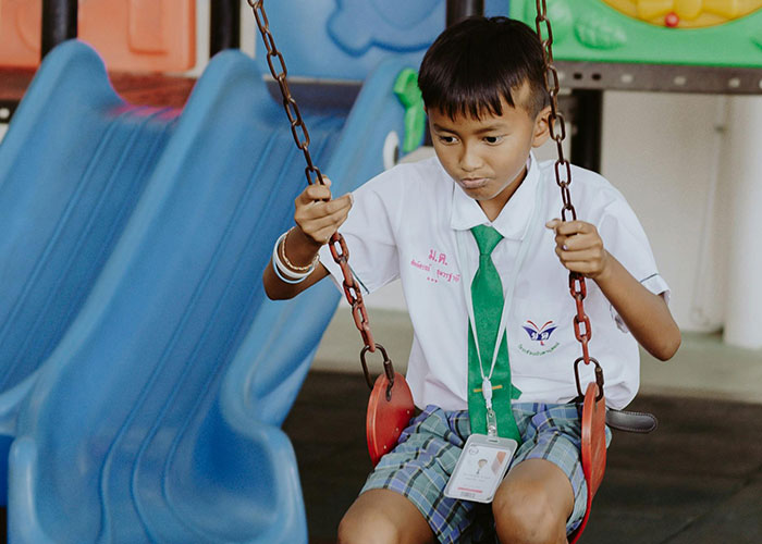 Child in school uniform sitting on a swing at a playground, showcasing kids with no filter moments.