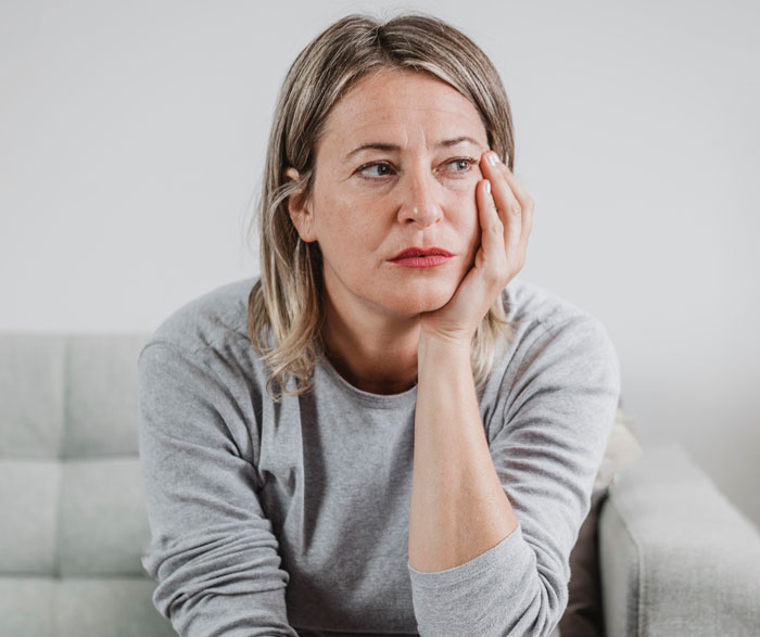 Woman sitting on a couch looking thoughtful and concerned about emptying father's estate and will issues.