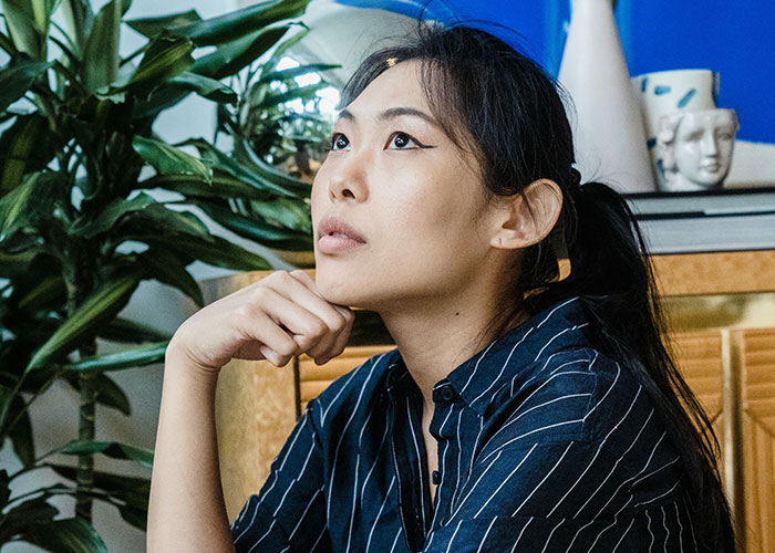 Young woman in a striped shirt sitting thoughtfully indoors, reflecting on experiences related to being neurodivergent.