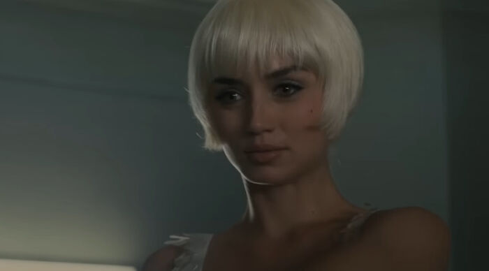 Young woman with platinum bob in dim room, contemplative expression, Would You Rather theme