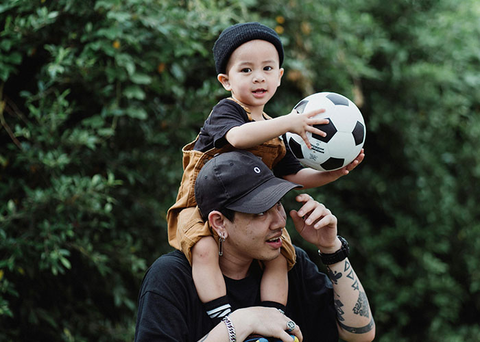Man carrying child holding soccer ball on shoulders, illustrating emotions tied to not being the biological parent.