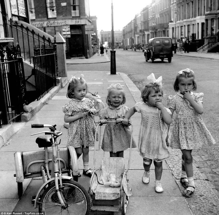 Four young girls in vintage dresses playing on a city sidewalk, capturing a moment in the history of humanity.