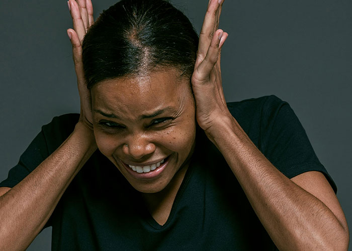 Person with a distressed expression covering ears, representing common habits neurodivergent people thought were normal.