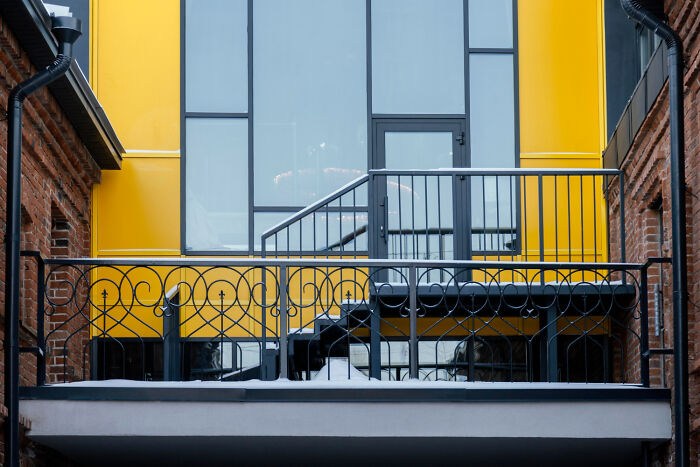 Modern yellow building facade with balcony railing between brick walls, illustrating weird satisfying situations not my problem anymore.