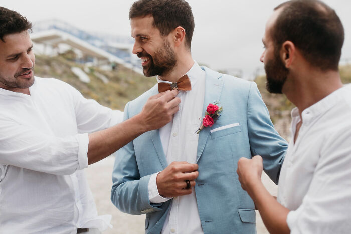 Groom smiling as friends adjust his bow tie and jacket, capturing one of the fastest times couples said I do moments.