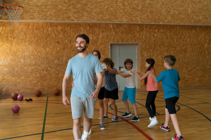 High school gym class with a teacher leading children playing games, showing education and lively school activities.