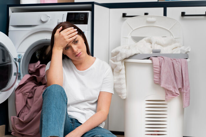 Woman looking stressed sitting on the floor by laundry machines and a hamper, illustrating fastest times couples separating.