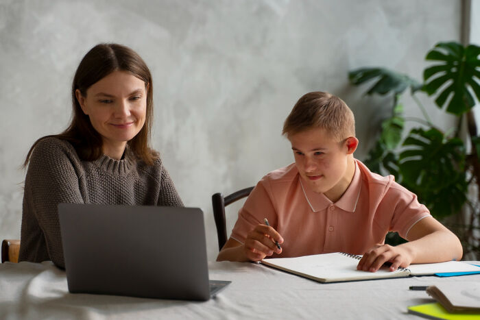 Young student with learning difficulties and tutor working together using a laptop, reflecting high school education challenges.
