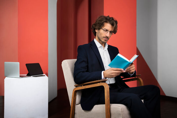 Man in a suit reading a book indoors, illustrating weird and shocking things people did in public with zero shame.
