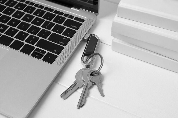 Silver keys on a keyring resting beside a laptop keyboard and stacked books, illustrating bizarre office rules concept.