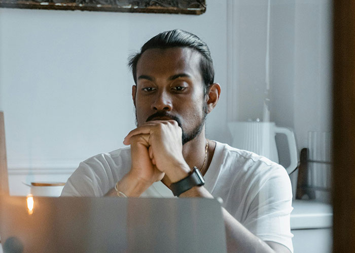Man in a white shirt looking thoughtful and concerned while reflecting on not being the biological parent at home.