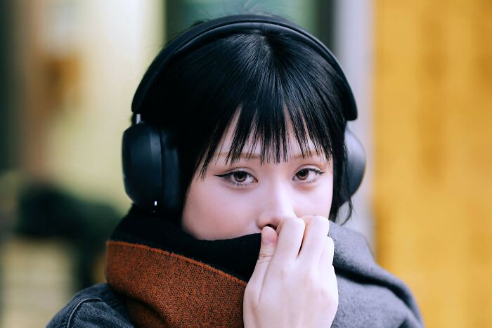 Young woman wearing headphones and a scarf, appearing thoughtful as viewers cast their vote on right decisions.