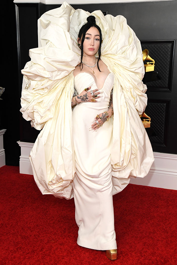 Woman in dramatic white gown with large ruffled sleeves posing on the red carpet at wild Grammys looks event.