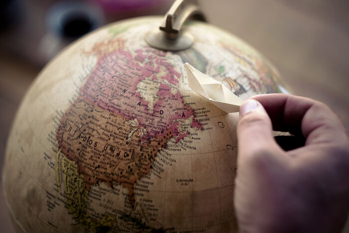 Hand placing a paper boat on a globe, symbolizing moments so ridiculous people thought they were being pranked.