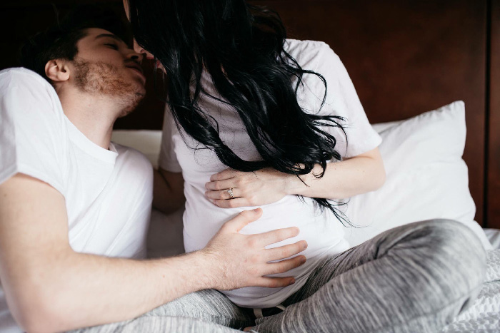 Pregnant couple cuddling on bed, man touching belly in intimate, creative maternity photoshoot idea