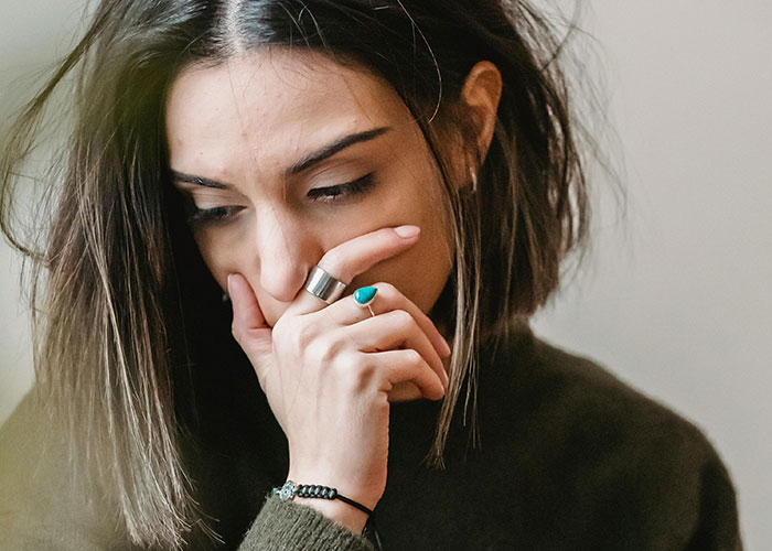 A thoughtful woman touching her face, reflecting on habits neurodivergent people thought were normal.