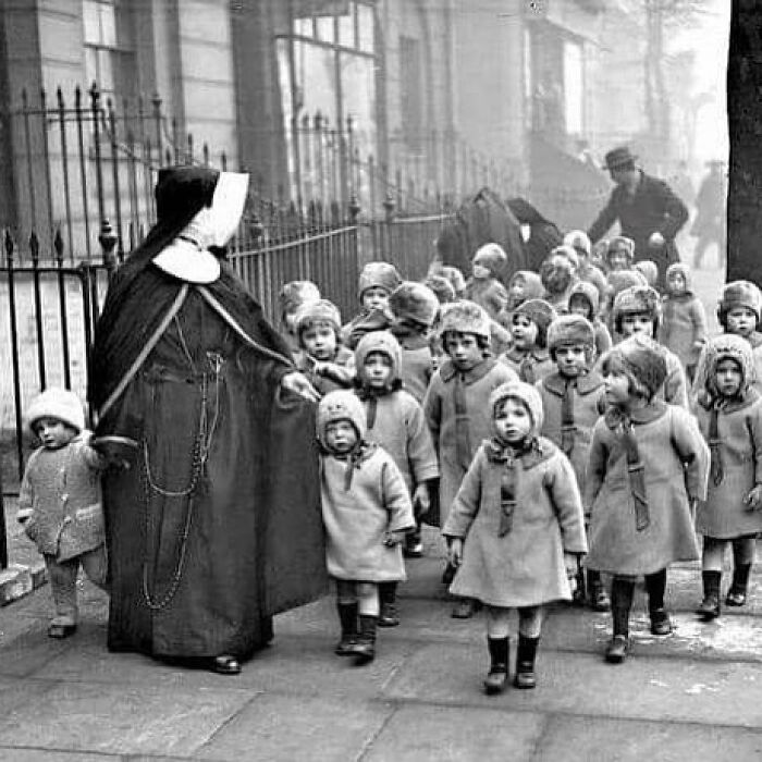 Black and white photograph showing a group of children walking with a nun, reflecting the history of humanity.