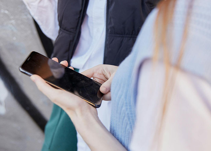 Person holding a smartphone with two people in casual clothes, illustrating neurodivergent habits in daily life.