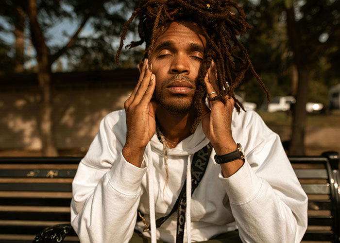 Young man with dreadlocks sitting outside on a bench, appearing thoughtful and reflecting on neurodivergent experiences.