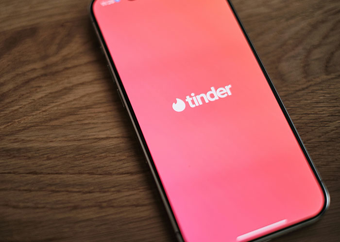 Smartphone displaying the Tinder app logo on a wooden surface, illustrating casual digital connections and social interaction.