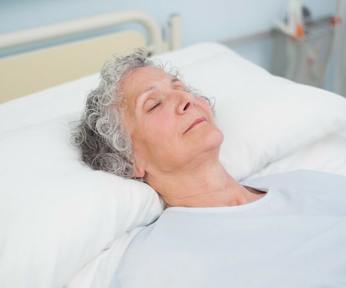 Elderly patient lying with eyes closed in hospital bed, a quiet scene familiar to hospital workers.