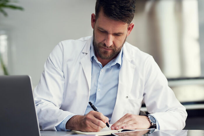 Doctor writing notes during patient consultation, representing an example of unethical behavior with a patient.