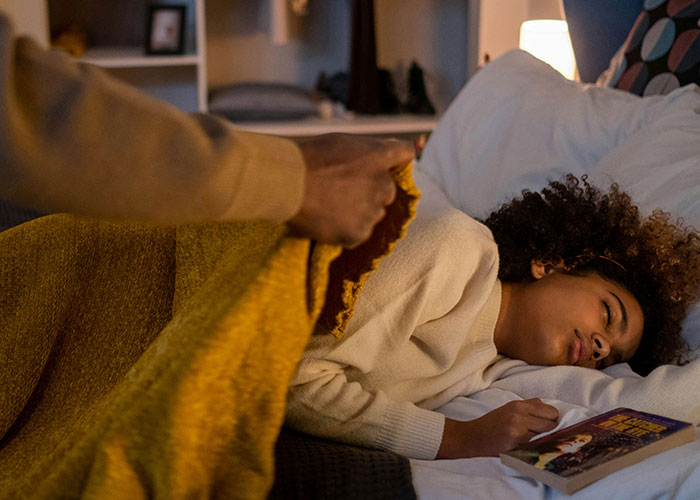 Man gently covering a sleeping child with a blanket, illustrating themes of family and non-biological parenthood.