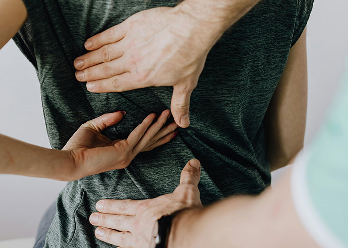 Hands performing a back examination on a person wearing a dark gray shirt, representing neurodivergent habits awareness.